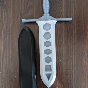 May include: A silver-colored plastic sword with a hexagonal design on the blade and a black plastic sheath.