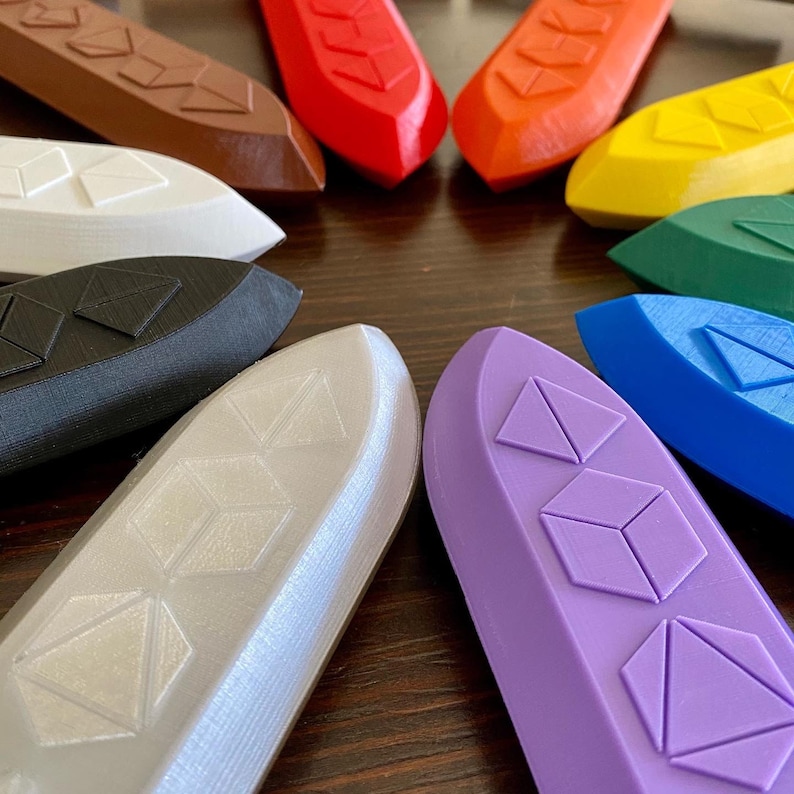 May include: A set of 10 colorful, geometrically patterned, 3D printed boat-shaped objects. The objects are arranged in a circle on a wooden surface.