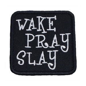 May include: Black square patch with the words "WAKE PRAY SLAY" embroidered in white. The patch has a black border and rounded corners. The text is in a bold, stylized font.