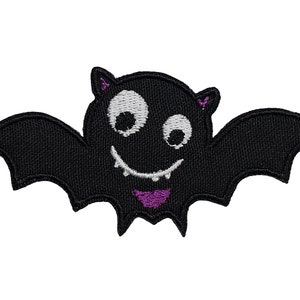 Può includere: Una toppa da stirare ricamata nera di un pipistrello dei cartoni animati con occhi bianchi e una bocca viola. Il pipistrello sta sorridendo.