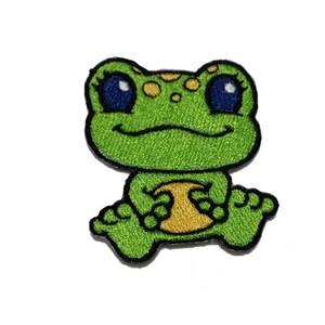 May include: Green embroidered frog patch with yellow spots and big blue eyes. The frog is sitting with its legs crossed and has a yellow belly.