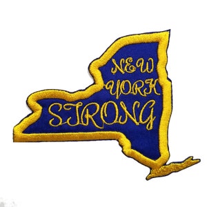 Op de afbeelding: Een geborduurde patch in blauw en goud in de vorm van de staat New York met de tekst "New York Strong" in goud.