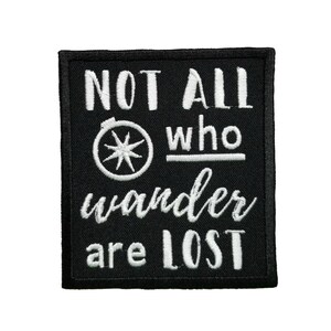 Może przedstawiać: Czarna naszywka haftowana z białym tekstem, który brzmi "Not all who wander are lost". W projekcie znajduje się symbol kompasu.