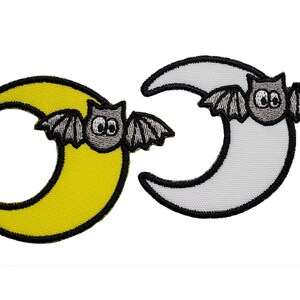 Può includere: Due toppe a forma di luna crescente con un pipistrello su ciascuna. Una luna è gialla e l'altra è bianca.