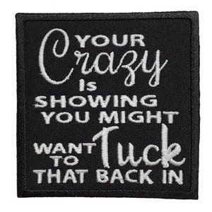 Puede incluir: Parche cuadrado negro con texto bordado en blanco: "YOUR Crazy IS SHOWING YOU MIGHT WANT TO Tuck THAT BACK IN". El parche tiene una apariencia texturizada.
