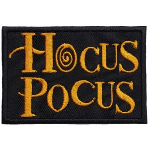 May include: A black embroidered patch with the words "Hocus Pocus" in gold thread.