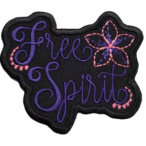 May include: Black embroidered patch with the words "Free Spirit" in purple script, and a purple and pink flower design. The patch has a black border and is suitable for clothing or accessories.