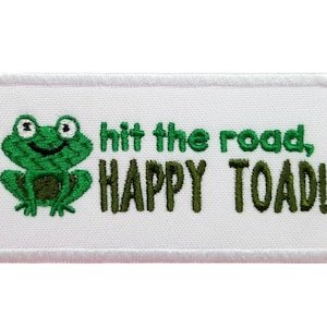 May include: White embroidered patch with a green frog and the text "hit the road, HAPPY TOAD!"