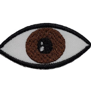 May include: Brown embroidered eye patch with a white iris and black pupil. The eye patch is surrounded by a black outline.