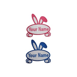 Op de afbeelding: Twee geborduurde strijkpatches met een konijn met een wit ovaalvormig lichaam. De bovenste patch is roze en de onderste patch is blauw. Beide patches hebben de tekst "Your Name" in het ovaal.