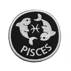 May include: A round, black embroidered patch featuring the Pisces zodiac symbol. Two white fish face each other, with a white astrological symbol between them. The word "PISCES" is embroidered in white below the fish.