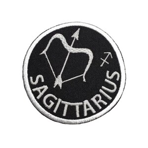 May include: Black and white embroidered patch with the zodiac sign Sagittarius. The patch features a bow and arrow with the word "Sagittarius" written around the outside.