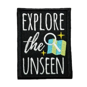 May include: Black embroidered patch with white text that reads "Explore the Unseen". A magnifying glass with a blue and yellow map inside is above the text. Two small yellow stars are on either side of the magnifying glass.