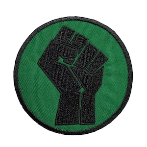 May include: A green circular patch with a black raised embroidered fist.