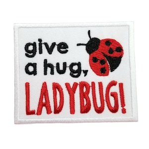 Peut inclure: Patch brodé blanc avec une coccinelle rouge et le texte "give a hug, LADYBUG!"
