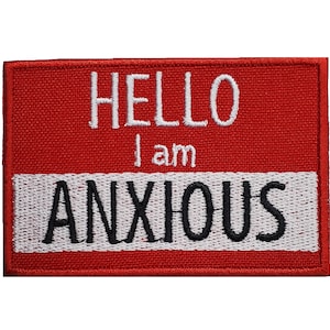May include: Red fabric name tag with white stitching and black text that reads "HELLO I am ANXIOUS".