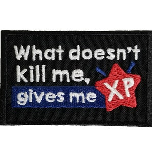 May include: Black embroidered patch with white text that reads "What doesn't kill me, gives me XP" with a red star with white text that reads "XP".