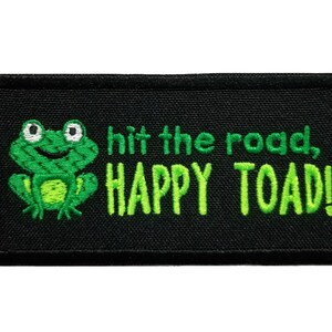 May include: Black embroidered patch with a green cartoon frog and the text "hit the road, HAPPY TOAD!"