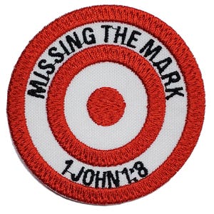 May include: Red and white embroidered patch with a bullseye target design. The text "MISSING THE MARK" is written around the outer edge of the target. The text "1 JOHN 1:8" is written below the target.