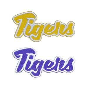 May include: Two embroidered iron-on patches with the word "Tigers" in a white outline. The top patch is yellow with white lettering. The bottom patch is purple with white lettering.