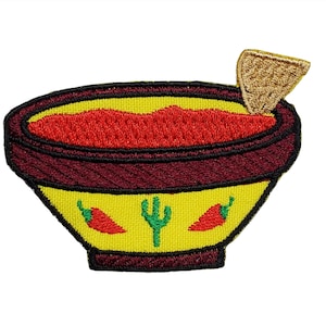 Puede incluir: Parche bordado de un tazón amarillo lleno de salsa roja y una tortilla amarilla. El tazón tiene diseños de cactus verdes y chiles rojos.
