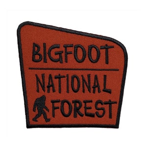 Può includere: Una toppa marrone con testo nero che recita "BIGFOOT NATIONAL FOREST" e una silhouette nera di Bigfoot che cammina verso destra.