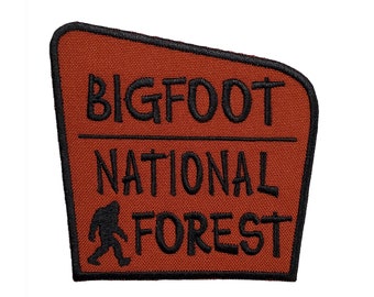 May include: A brown patch with black text that reads "BIGFOOT NATIONAL FOREST" and a black silhouette of a Bigfoot walking to the right.