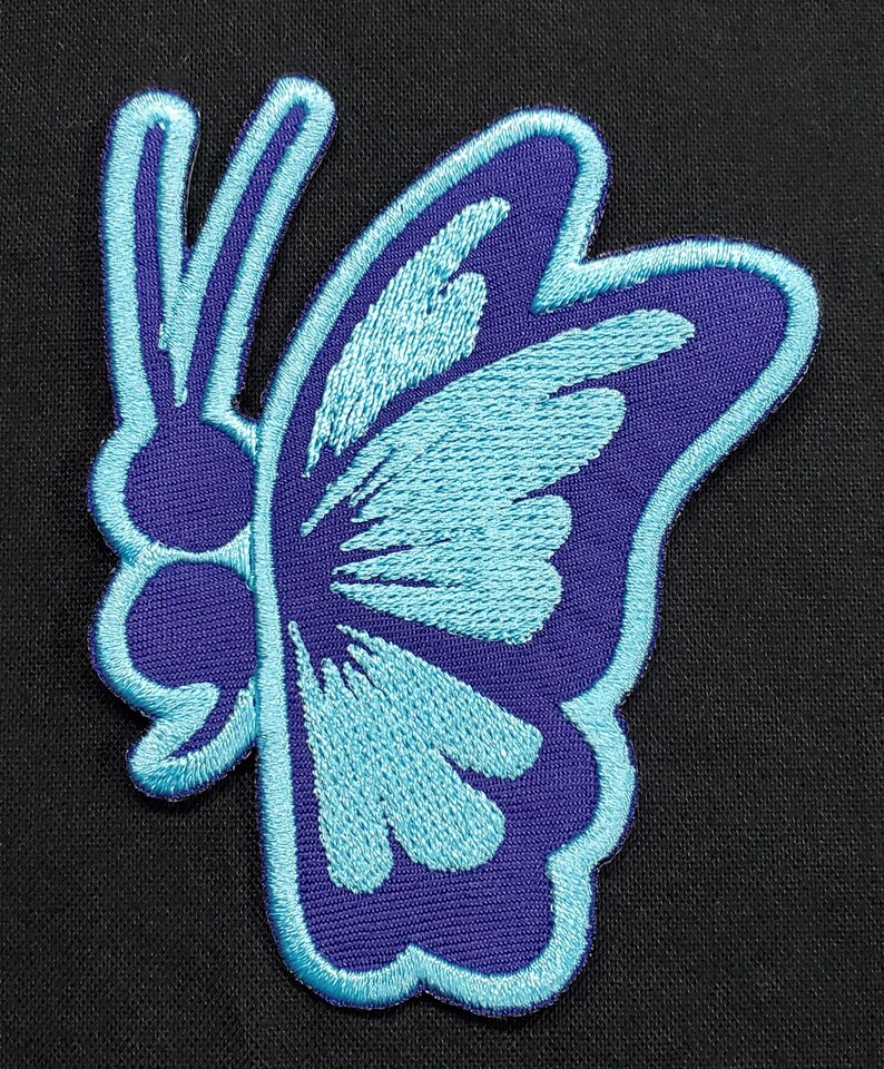 May include: Embroidered butterfly patch in shades of blue and purple. The butterfly design features a detailed wing pattern and a light blue outline. The patch is likely for clothing or accessories.