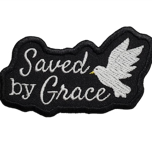 May include: Black embroidered patch with a white dove and the text "Saved by Grace".