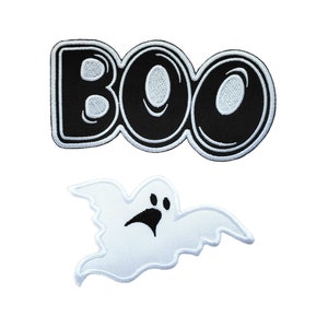 Può includere: Due toppe da stirare per Halloween. Una è in bianco e nero e dice "BOO" in un font da cartone animato. L'altra è un fantasma bianco con occhi neri e una bocca.