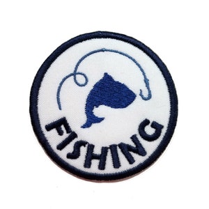 May include: A white circular patch with a black border and the word "FISHING" in black embroidery. A blue silhouette of a fish with a fishing hook is in the center.