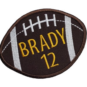 May include: Brown and white embroidered patch shaped like a football with the name "BRADY" and the number "12" in yellow thread.