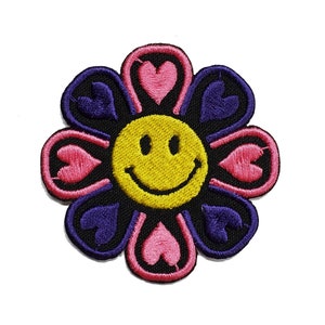 May include: A purple and pink flower with a yellow smiley face in the center. The flower has eight petals, each with a heart shape.