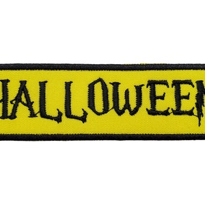 Puede incluir: Un parche rectangular amarillo con borde negro y la palabra "HALLOWEEN" en letras negras.