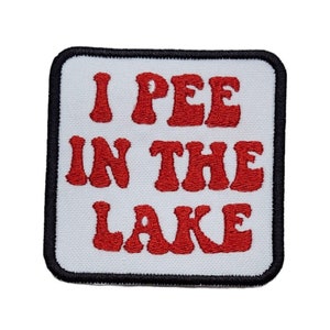 May include: White fabric patch with black stitching around the edges. The patch has red embroidered text that reads "I PEE IN THE LAKE".