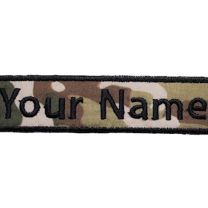 May include: A black embroidered name tag with the text "Your Name" on a camouflage background.