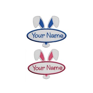 Op de afbeelding: Geborduurde patches met konijnenoren en een ovaal met de tekst "Your Name". Eén patch heeft blauwe oren en tekst, de andere heeft roze oren en tekst. Beide staan op een witte achtergrond.