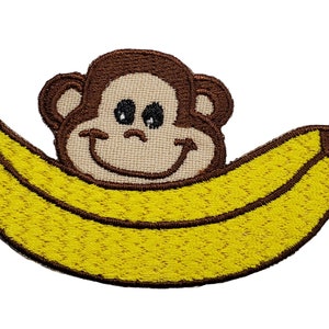 May include: Embroidered patch of a brown monkey with a smiling face, sitting inside a yellow banana.