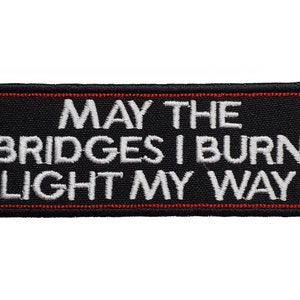 Puede incluir: Parche bordado negro con costuras rojas. El texto en el parche dice "May the bridges I burn light my way."