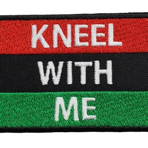 以下が含まれることがあります： 赤、黒、緑のパッチで、「Kneel With Me」という文字が白で書かれています。