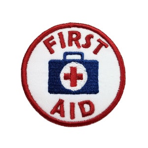 May include: A white circular patch with a red border. The text "FIRST AID" is in red lettering. A blue and white first aid kit with a red cross is in the center.