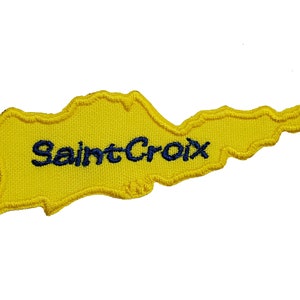 May include: Yellow felt outline of the island of Saint Croix with the text "Saint Croix" embroidered in blue thread.