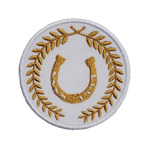 May include: A white embroidered patch with a gold horseshoe inside a wreath of gold leaves.