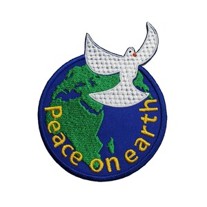 Pode incluir: Etiqueta bordada com uma pomba branca voando sobre um globo terrestre verde e azul. O texto "Peace on Earth" está escrito em amarelo ao redor do globo.