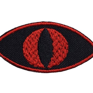 May include: Red embroidered eye patch with a black pupil. The eye patch is shaped like an almond and has a black outline.