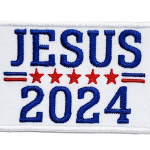 Könnte beinhalten: Weißer gestickter Aufnäher mit blauem Text, der "JESUS 2024" lautet. Unter dem Text befinden sich fünf rote Sterne und zwei rote Streifen.