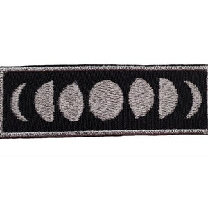 May include: Black and white embroidered patch with a series of moon phases in a rectangular shape.