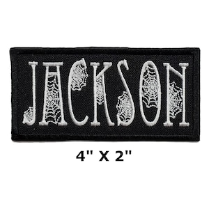 May include: Black embroidered patch with the word "JACKSON" in white with a spiderweb design. The patch is 4 inches by 2 inches.