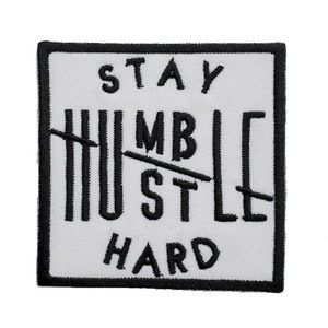 Könnte beinhalten: Ein quadratischer, weißer Aufnäher mit schwarzem, gesticktem Text und einem schwarzen Rand. Der Text lautet "STAY HUMBLE HUSTLE HARD", wobei die Wörter "HUMBLE" und "HUSTLE" mit schwarzen Linien durchgestrichen sind.