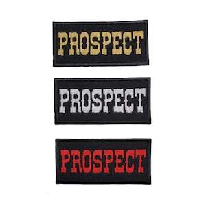 Puede incluir: Tres parches rectangulares negros con costuras blancas. Cada parche tiene la palabra "PROSPECT" bordada en hilo dorado, plateado y rojo.